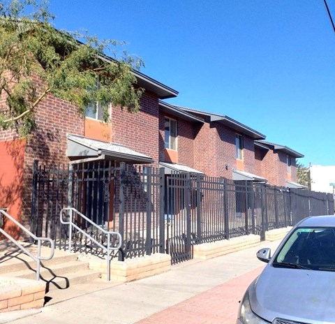 A brick building with a black iron fence and a silver car parked in front.