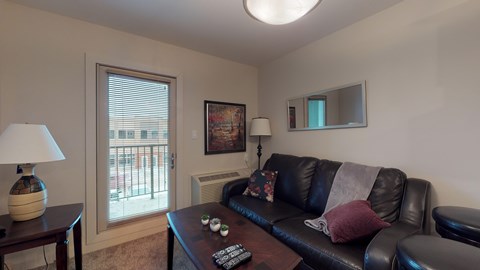A living room with a black couch and a lamp on a table.