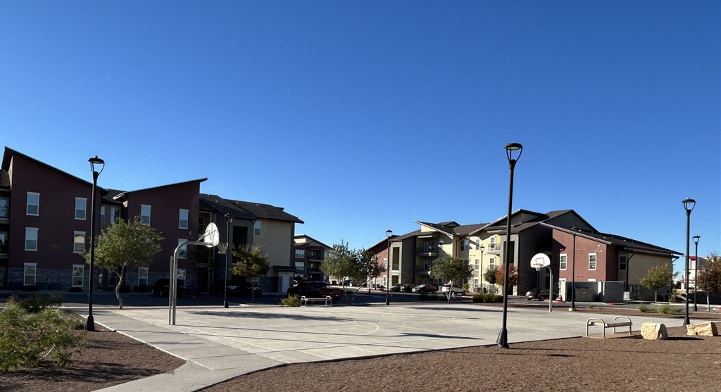 A sunny day at a park with a basketball court and apartment buildings in the background.