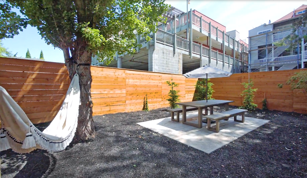 A backyard with a hammock, picnic table, and a tree.