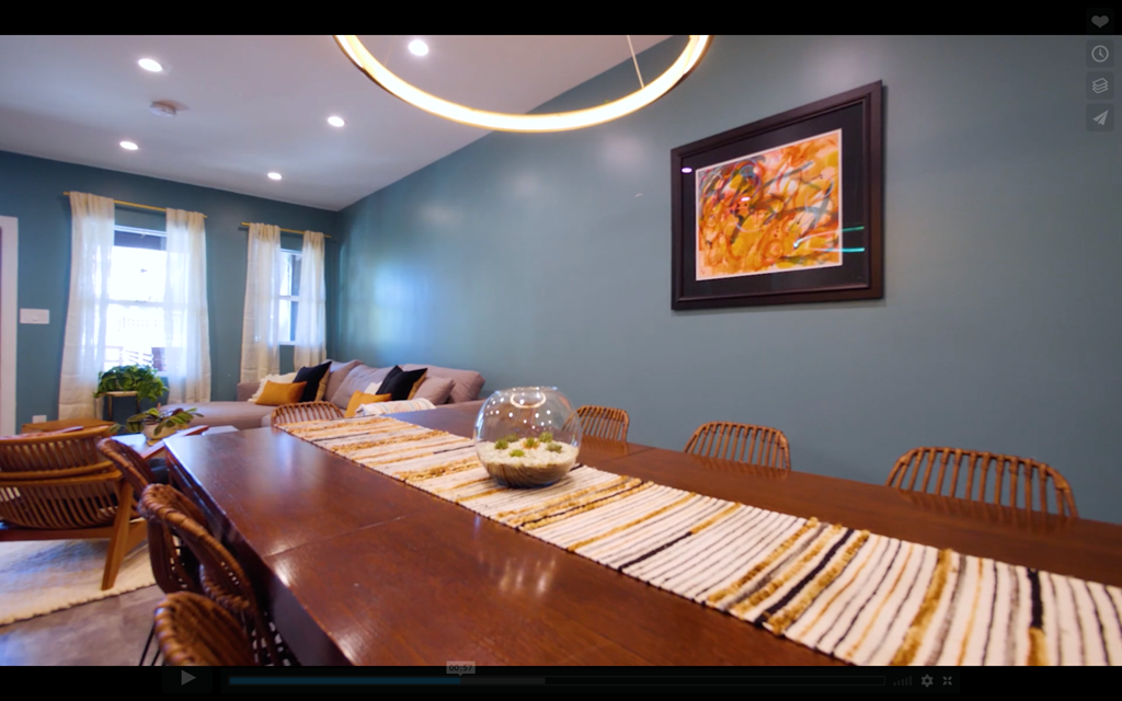 A long wooden table is surrounded by chairs in a room with a painting on the wall.