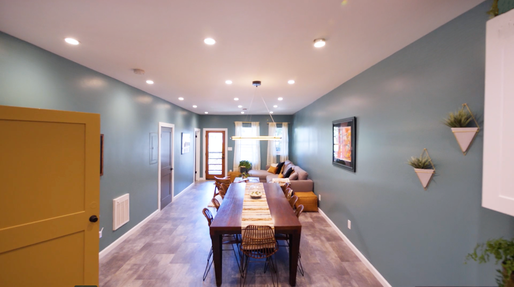 A long wooden table is surrounded by chairs in a room with a white ceiling.