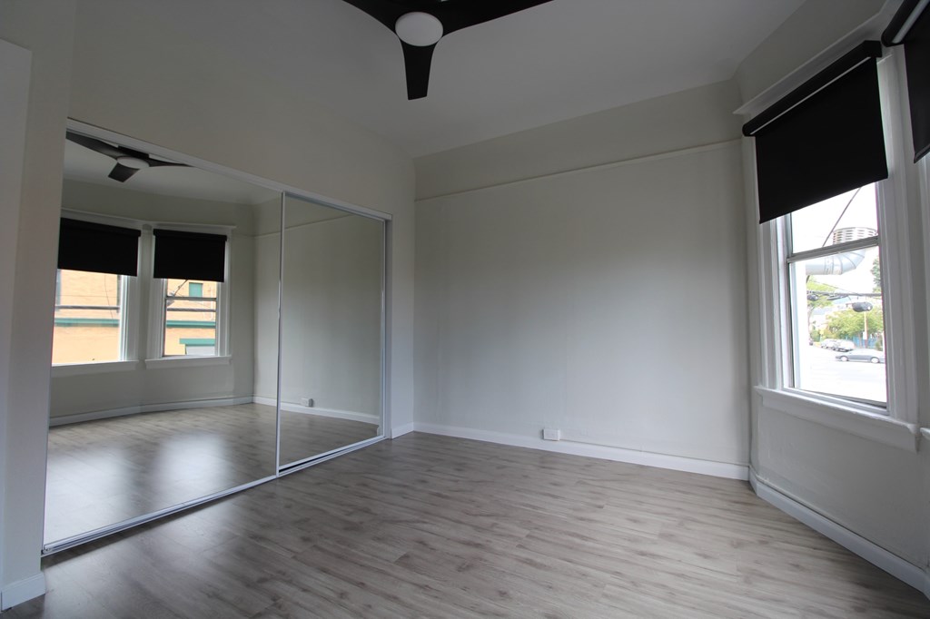 A room with a ceiling fan and large windows.