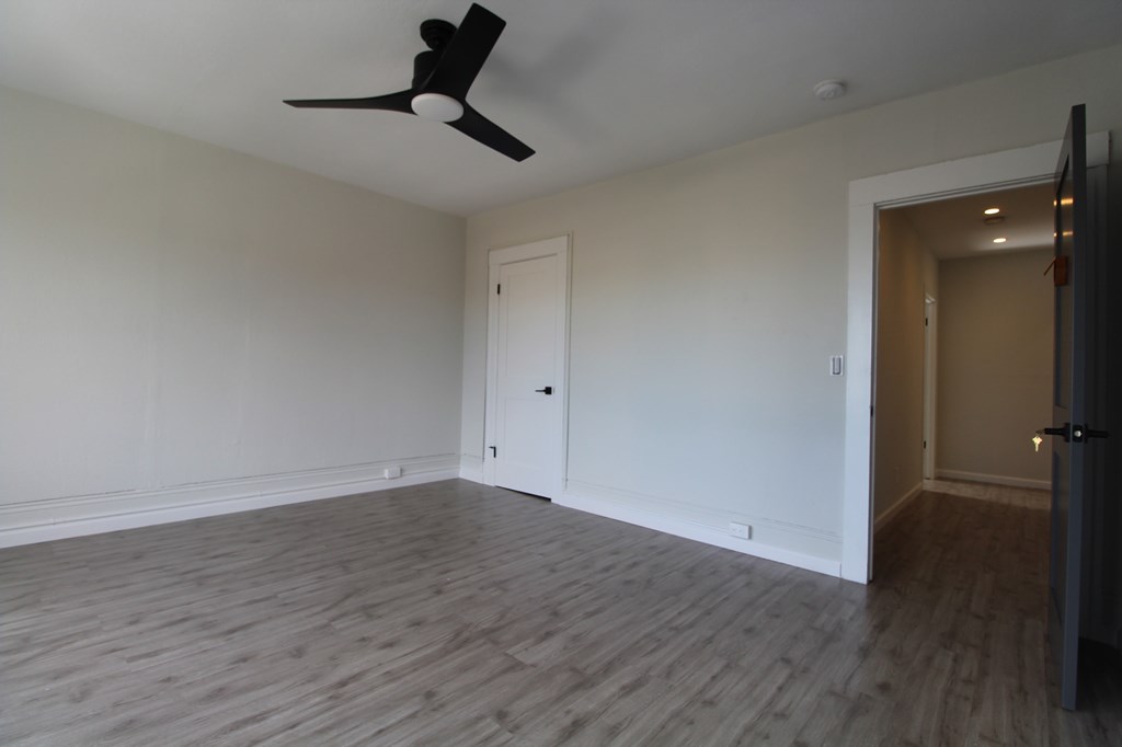 A room with a ceiling fan and light fixture, a door, and a wooden floor.