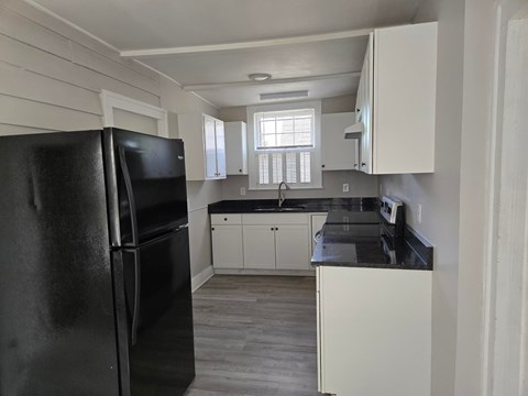 A black refrigerator is in a kitchen with white cabinets.