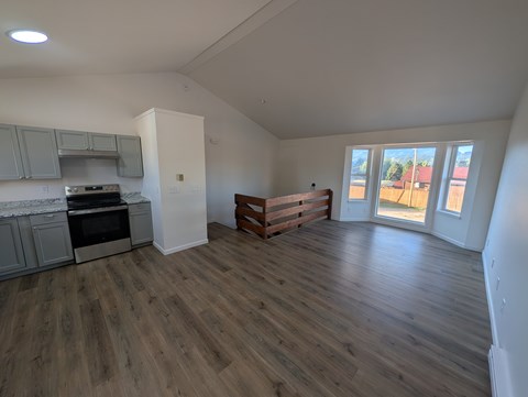 A spacious room with wooden flooring and a kitchen area with a stove and oven.