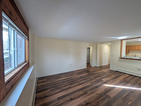 A room with wooden flooring and a large window on the left side.