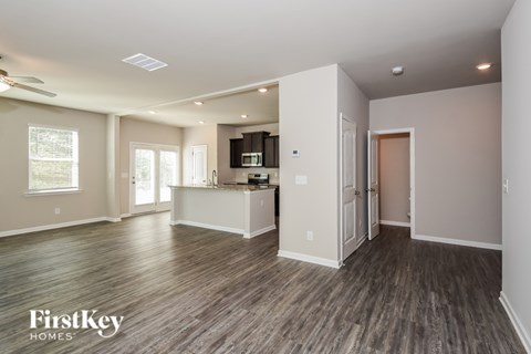 A spacious living room with wood flooring and a kitchen area in the background.