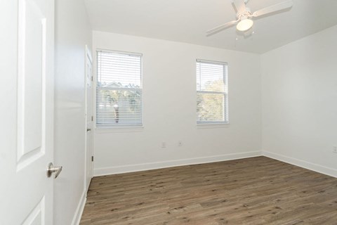 A room with a ceiling fan and two windows.