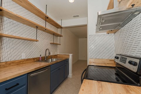 A kitchen with a black and white tiled backsplash and wooden shelves.