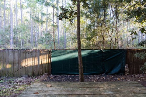 A wooden deck leads to a green tarp-covered area in a wooded area.