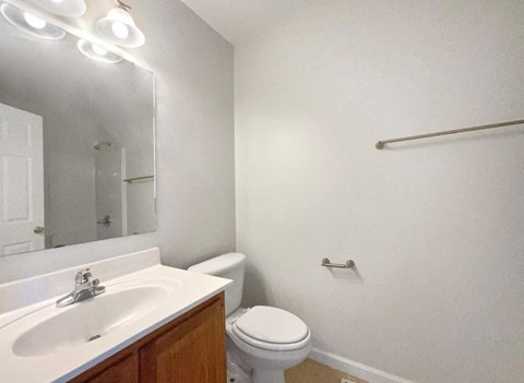 A white bathroom with a toilet, sink, mirror, and light fixture.