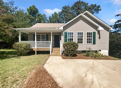 A small house with a porch and green shutters.