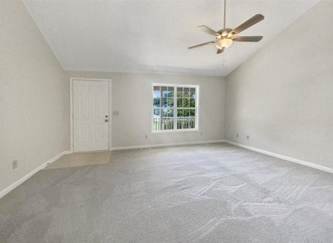 A room with a ceiling fan and a window with a view of trees.