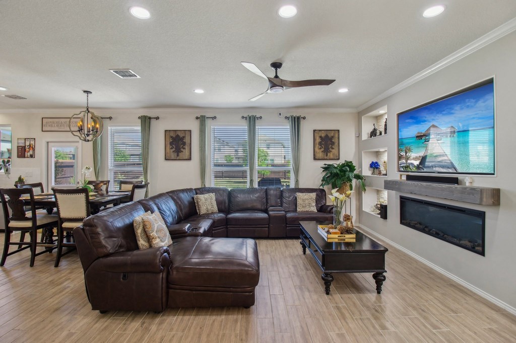 A living room with a brown leather couch and a flat screen TV mounted on the wall.