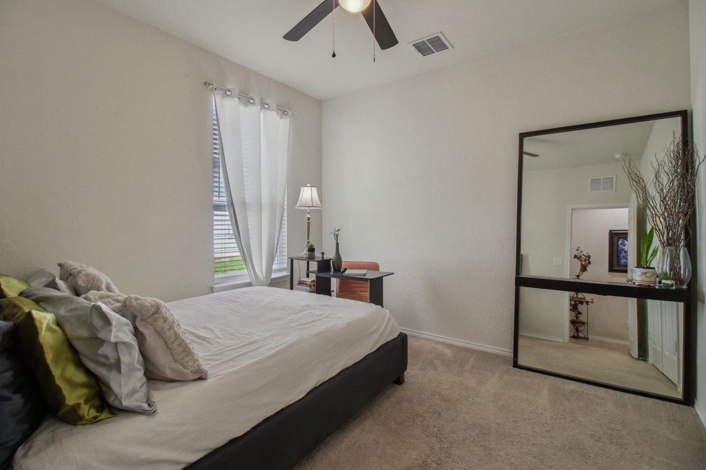 A bedroom with a bed, a mirror, and a ceiling fan.