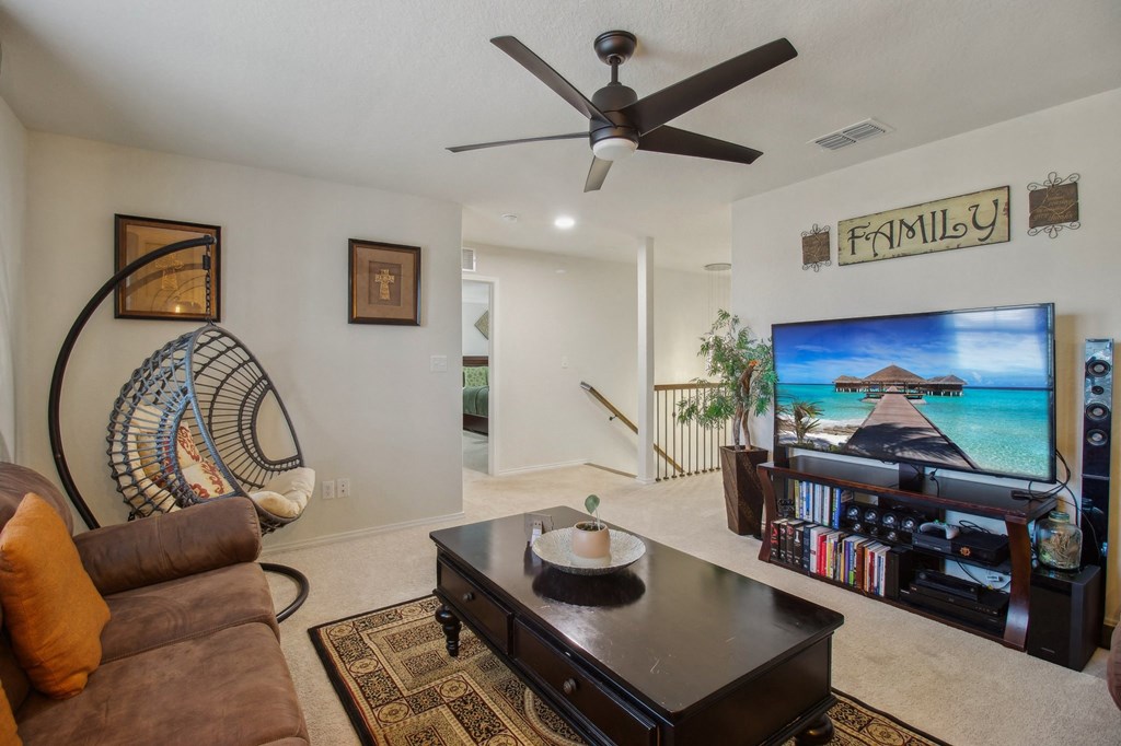 A living room with a brown sofa, a coffee table, a TV, and a ceiling fan.
