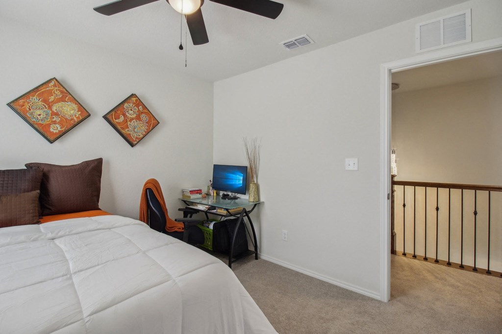 A bedroom with a bed, desk, and ceiling fan.
