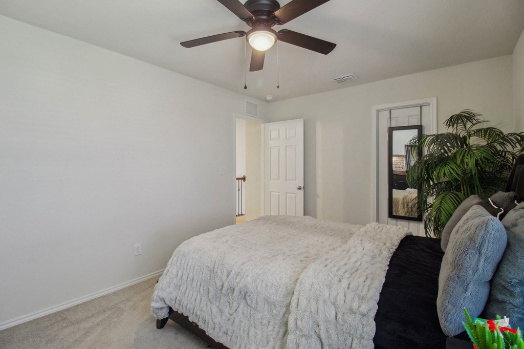 A bedroom with a bed, a ceiling fan, and a door.