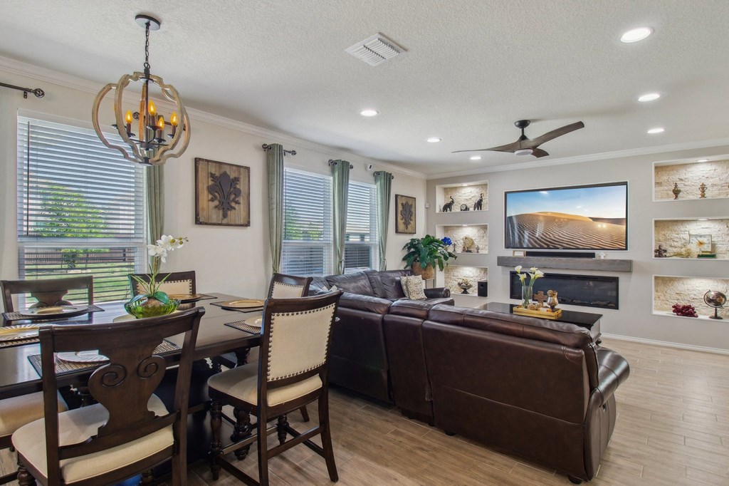 A living room with a brown couch, a dining table with chairs, and a television on the wall.
