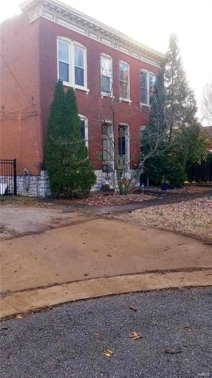 A red brick building with a black gate and a tree in front.