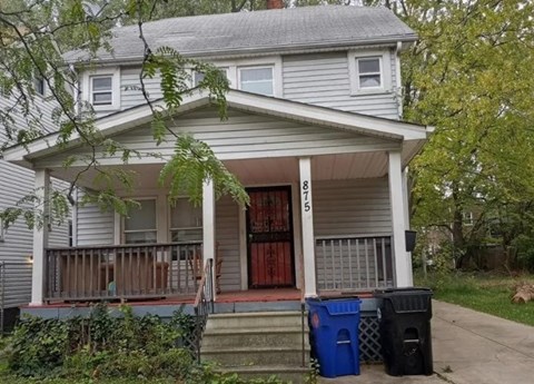 A house with a porch and two trash bins in front.