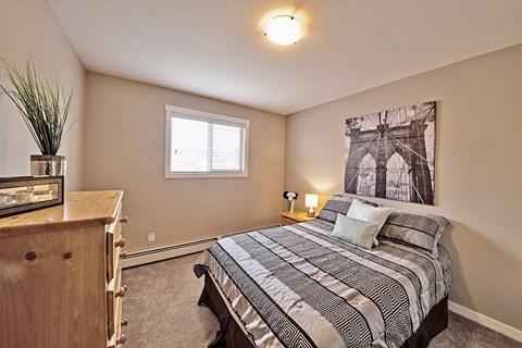 A bedroom with a bed, nightstand, and a plant.