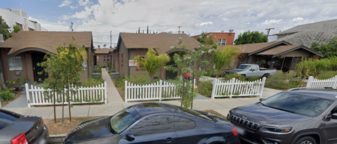 A car is parked in front of a house with a white picket fence.