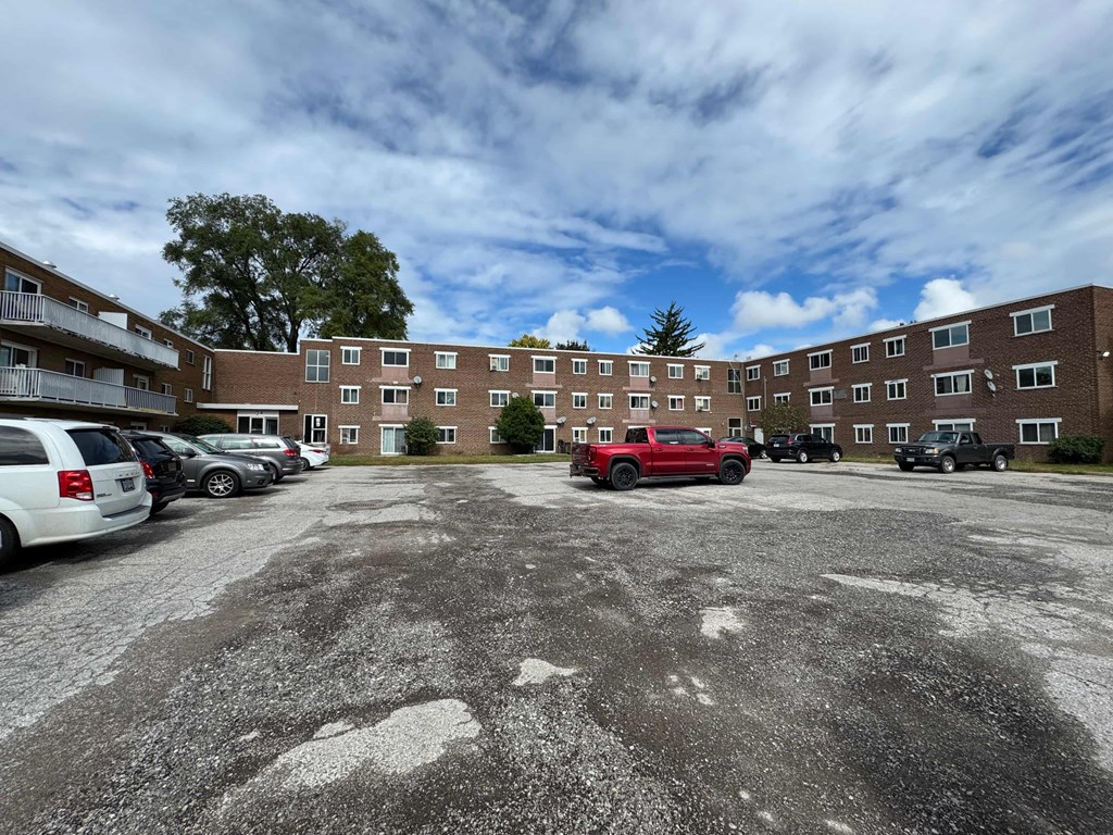 A parking lot with a red truck and several cars in front of a brick building.