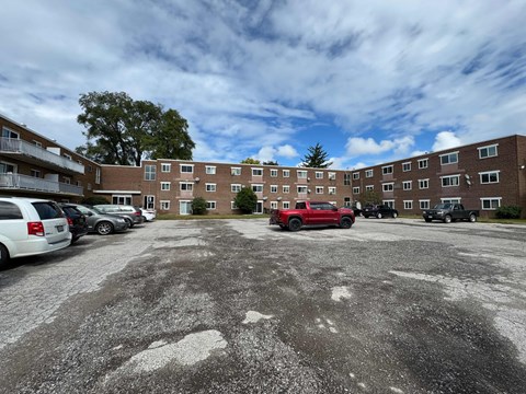 A parking lot with a red truck and several cars in front of a brick building.