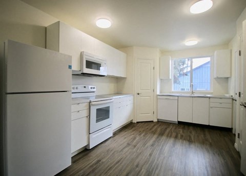 A kitchen with white appliances and wooden floors.