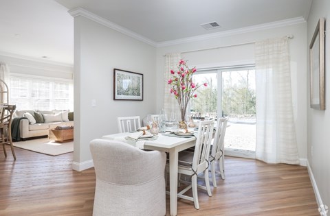 A dining room with a table set for two and a couch in the background.
