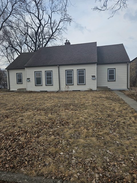 A small house with a grey roof and white walls is surrounded by a field of dry leaves.