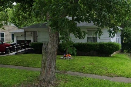 A tree stands in a grassy area in front of a house.
