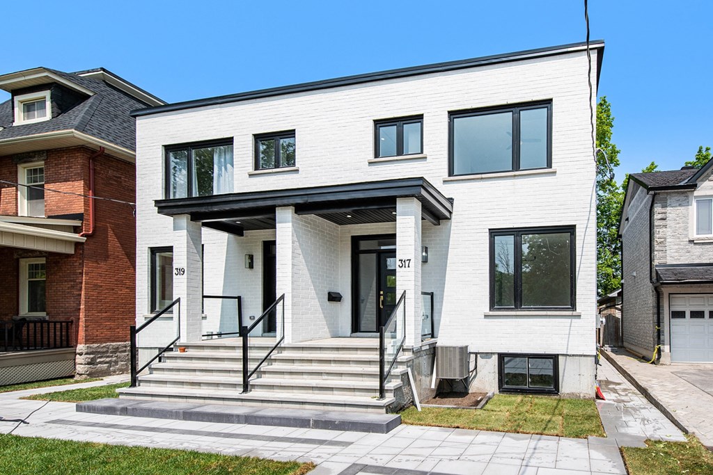 A white modern house with a black awning and a black railing on the steps.