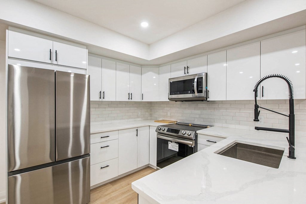 A modern kitchen with a stainless steel refrigerator, white countertops, and black appliances.