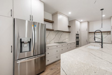 A modern kitchen with a stainless steel refrigerator and marble countertops.