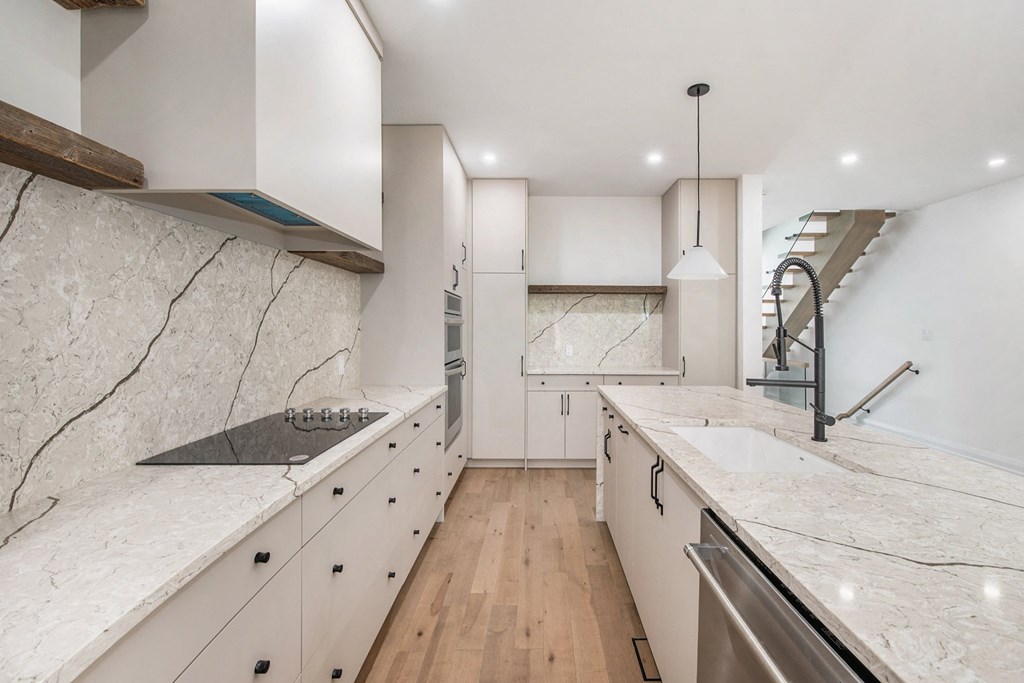 A modern kitchen with marble countertops and wooden floors.