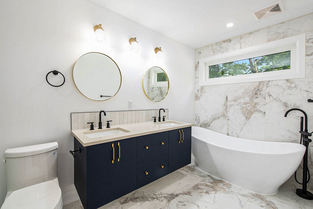 A white and marble bathroom with a black faucet and a white toilet.