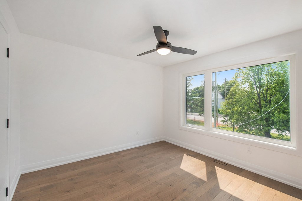 A room with a ceiling fan and a window showing trees outside.