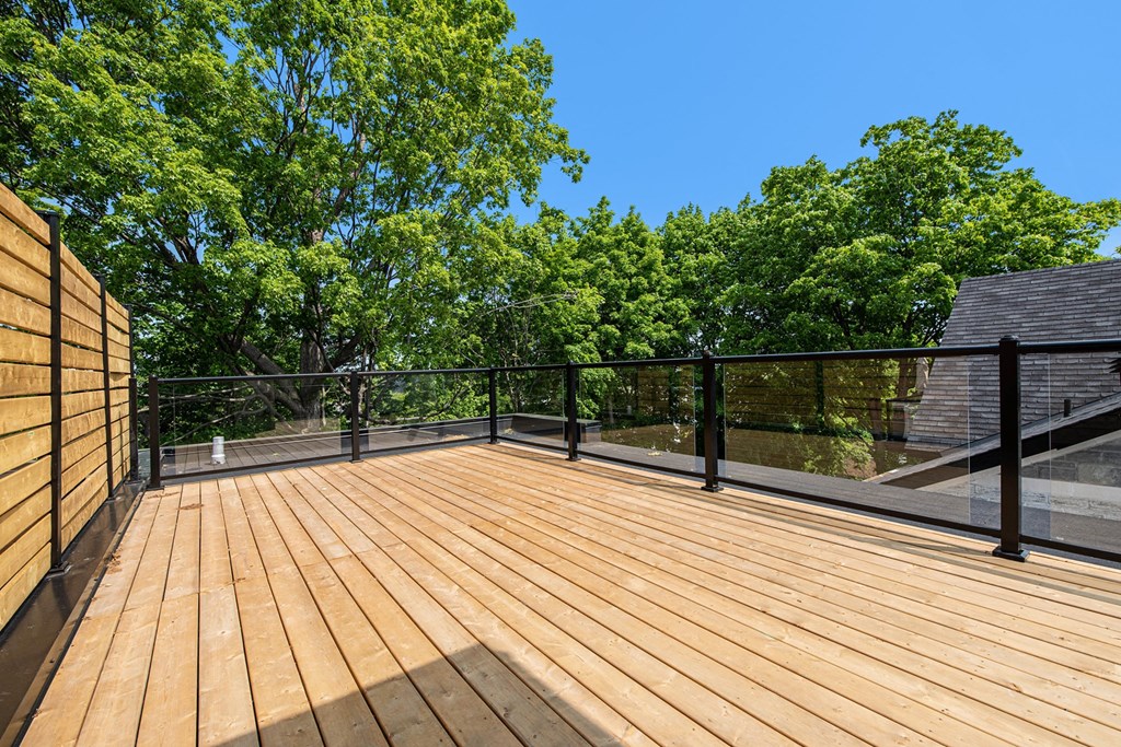 A wooden deck with a black railing and trees in the background.