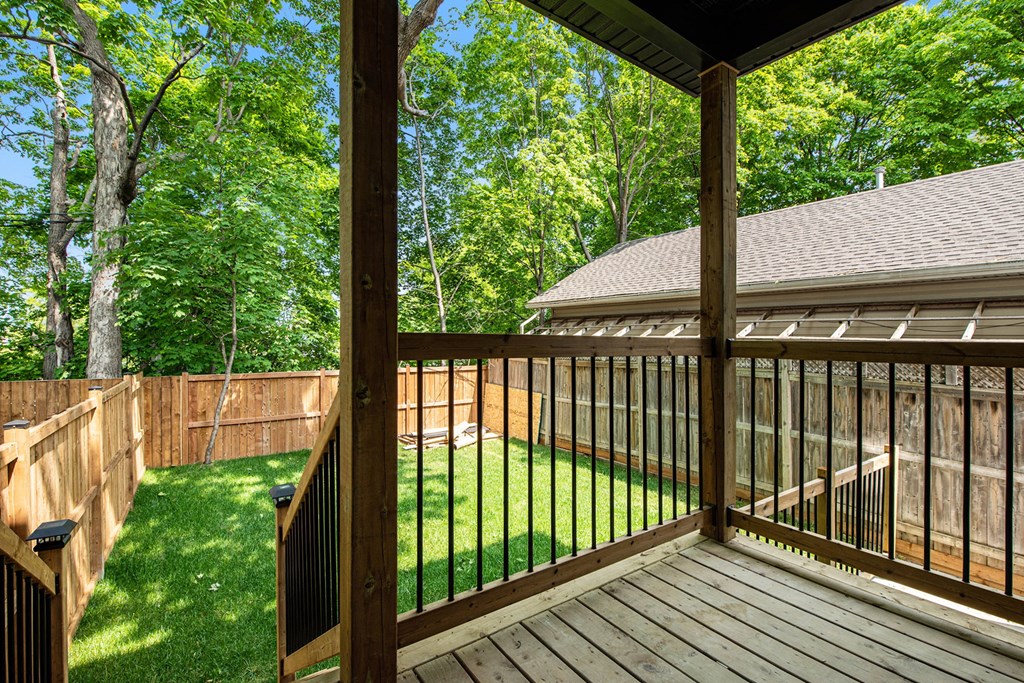 A wooden deck with a metal railing and a view of a backyard with a lawn and trees.