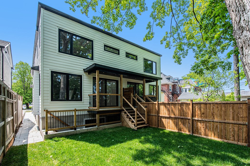 A green house with a wooden deck and a tree in front.