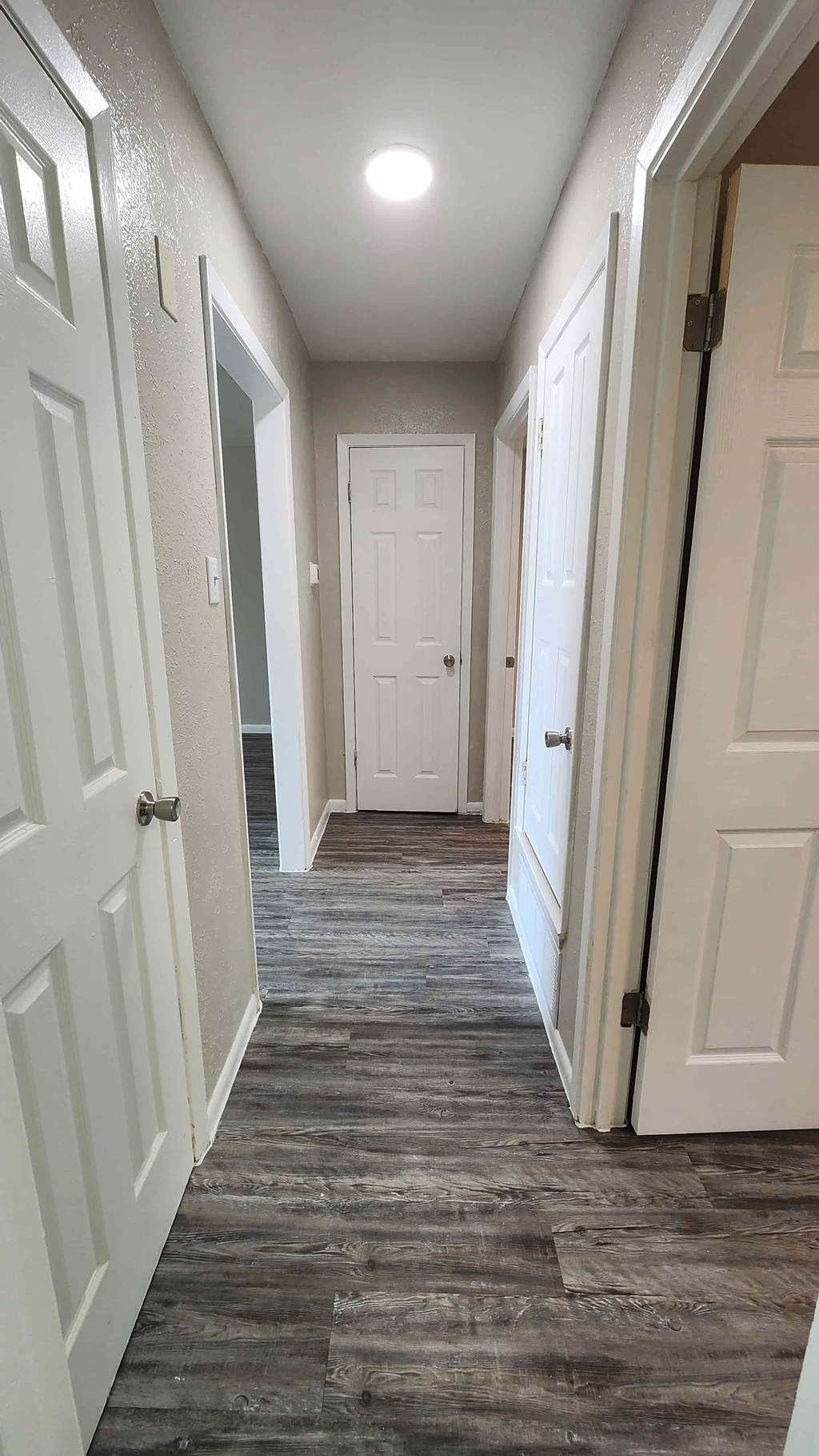 A long hallway with white doors and a wooden floor.