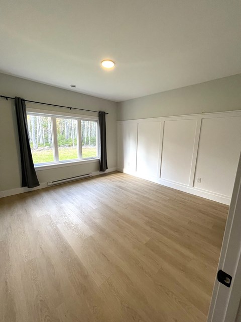 A room with wooden flooring and a window with a view of trees.