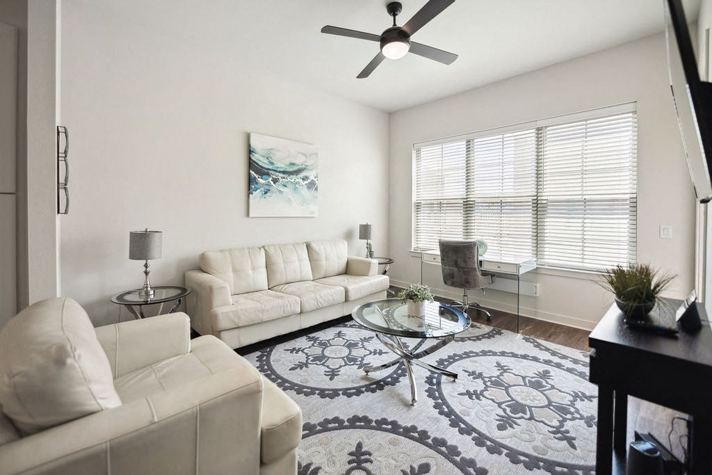 A living room with a white couch, a glass coffee table, and a ceiling fan.