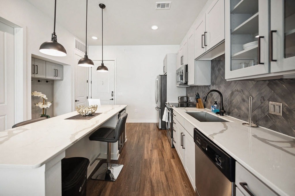 A modern kitchen with a long white island and stainless steel appliances.