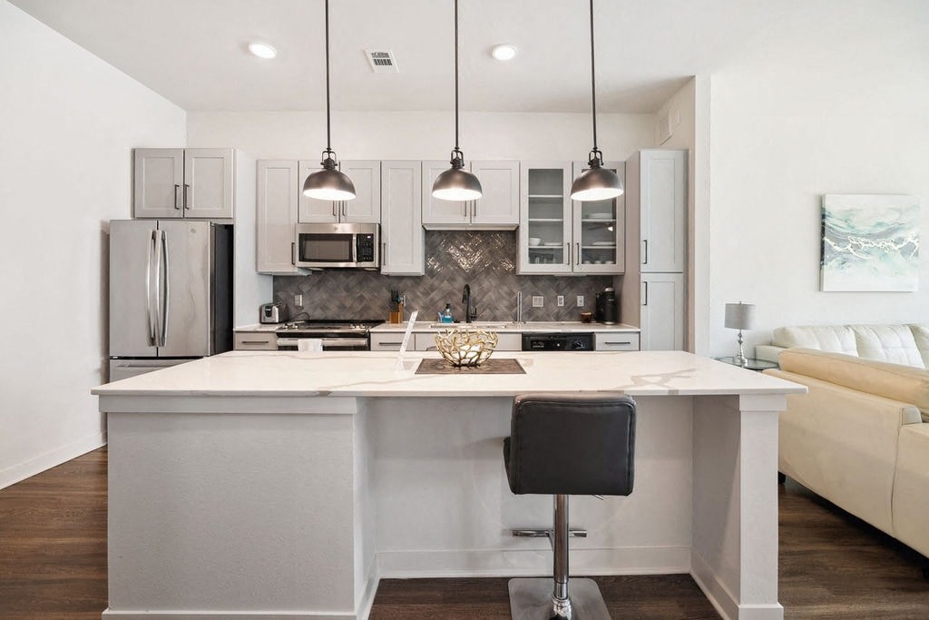 A modern kitchen with a white island and a black bar stool.