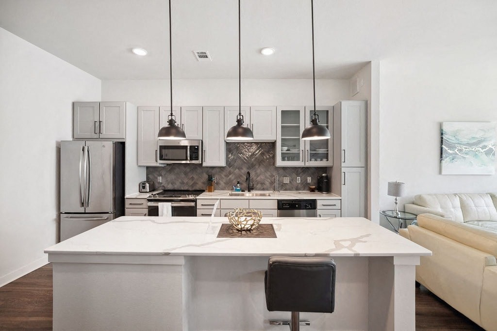 A modern kitchen with a white island and black chairs.