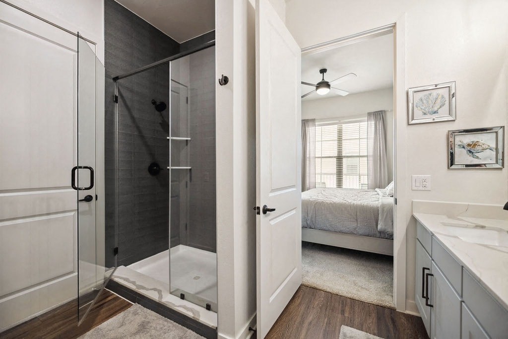 A bathroom with a walk-in shower and a bedroom with a bed and a ceiling fan.